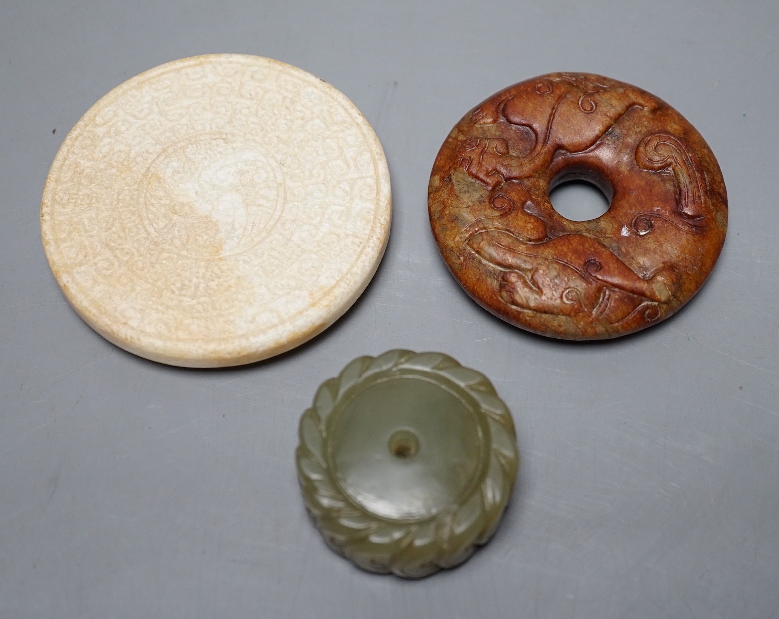 A Chinese green jade 'cash' pendant, a russet jade bi-disc and a burnt jade circular plaque